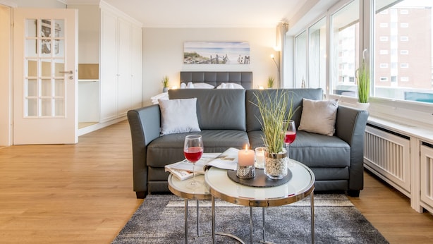 Een moderne woonkamer met een grijze bank, een ronde salontafel met kaarsen en een glas rode wijn.