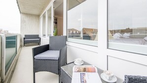 Een balkon met rieten meubilair, een tafel met een tijdschrift en een kop koffie.