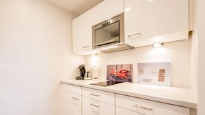 Een moderne keuken met witte kastjes, een roestvrijstalen oven en een aanrecht met een koffiezetapparaat en decoratieve objecten.