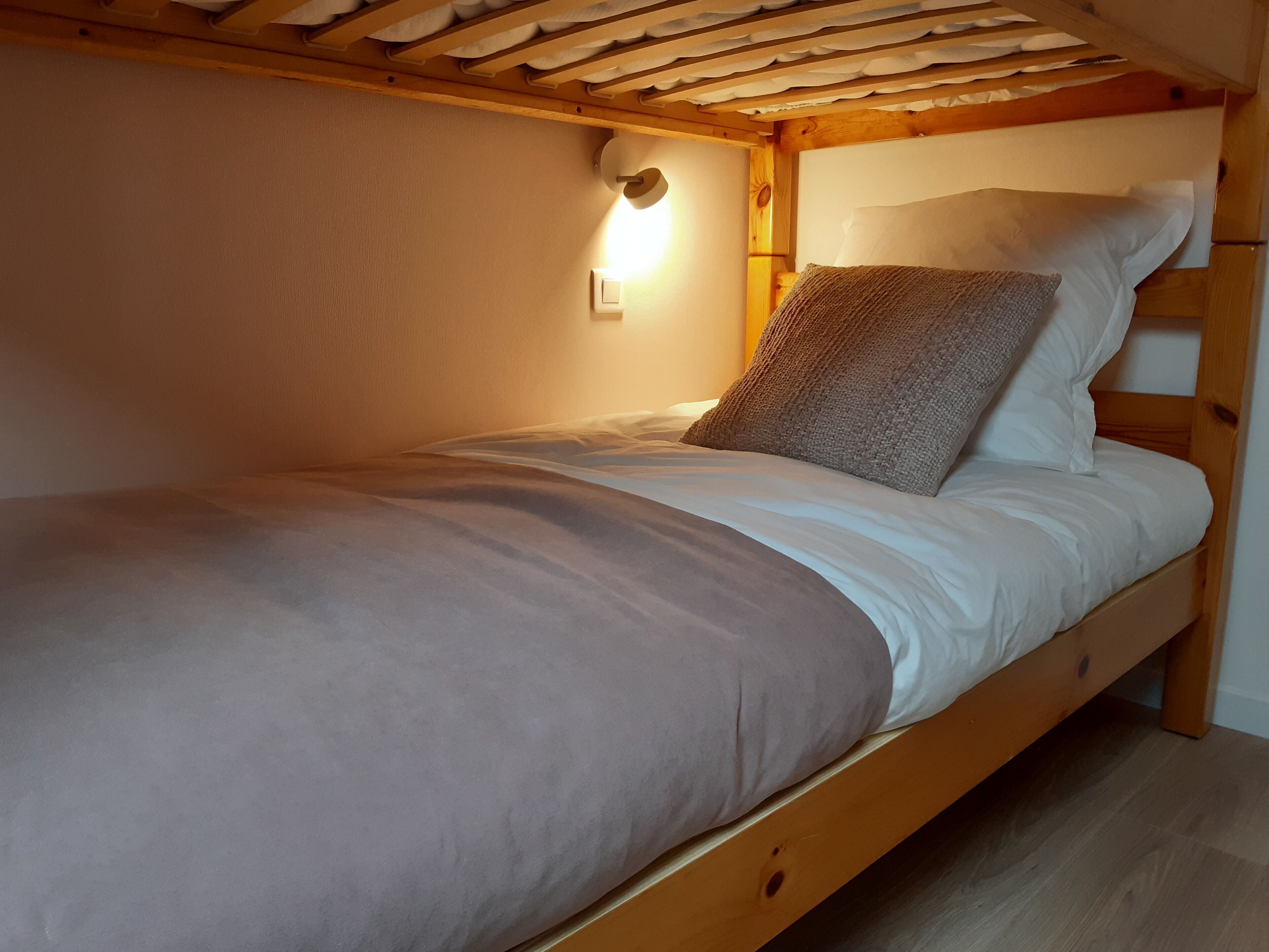 Un lit simple avec un cadre en bois, une literie blanche et un oreiller à texture.
