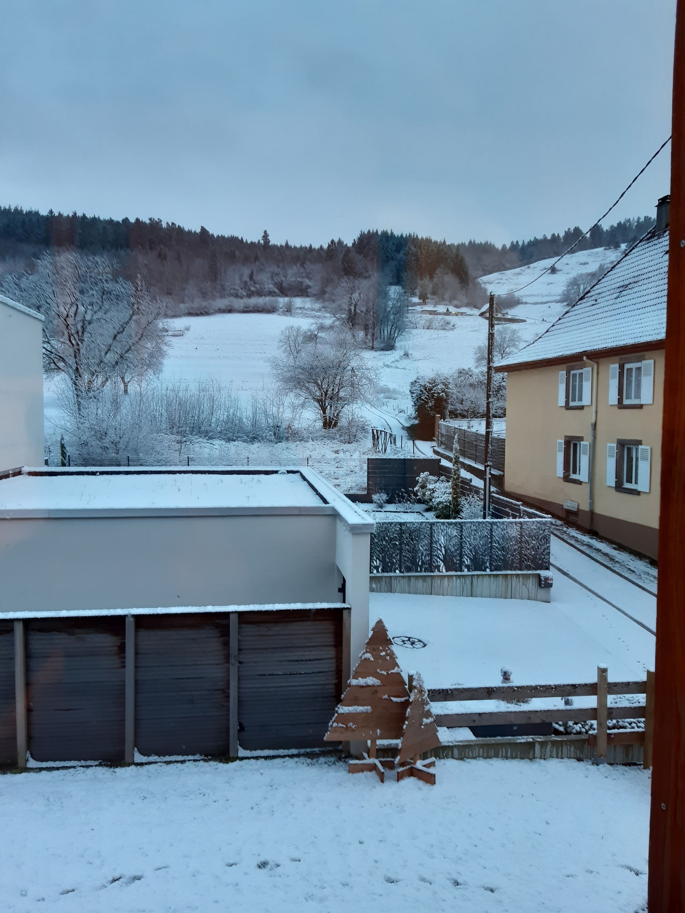A residential area with snow-covered ground, a small wooden Christmas tree, and houses with visible garages.