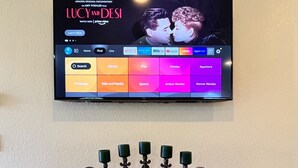 A flat-screen TV mounted on a wall displaying a documentary. Below the TV, there is an ornate, dark wooden console with decorative elements and a power outlet.