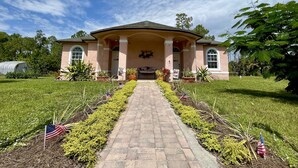 A house with a covered porch, a brick pathway leading to the entrance, and American flags placed in the garden.