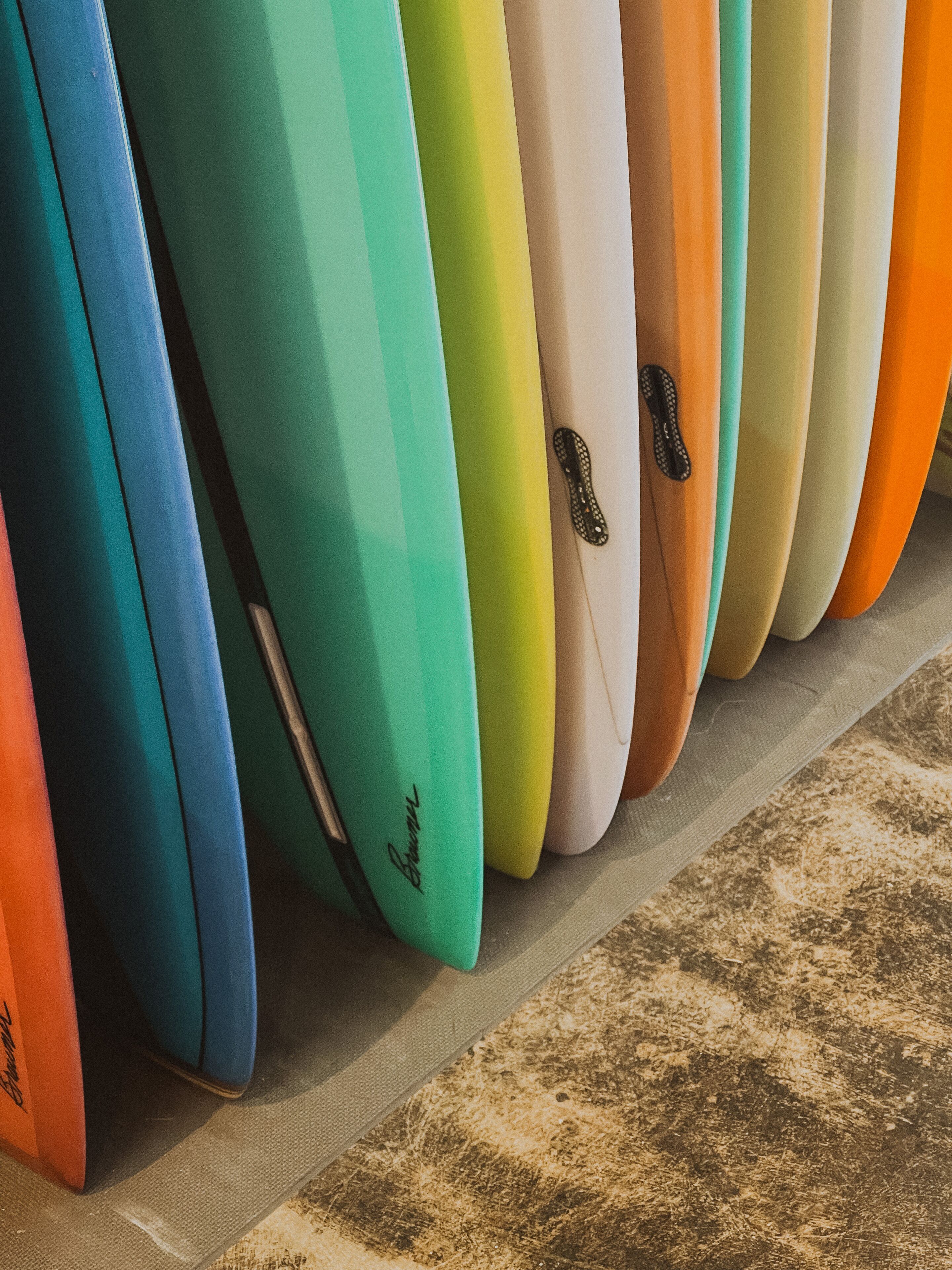 A row of surfboards with various colors and a textured floor.