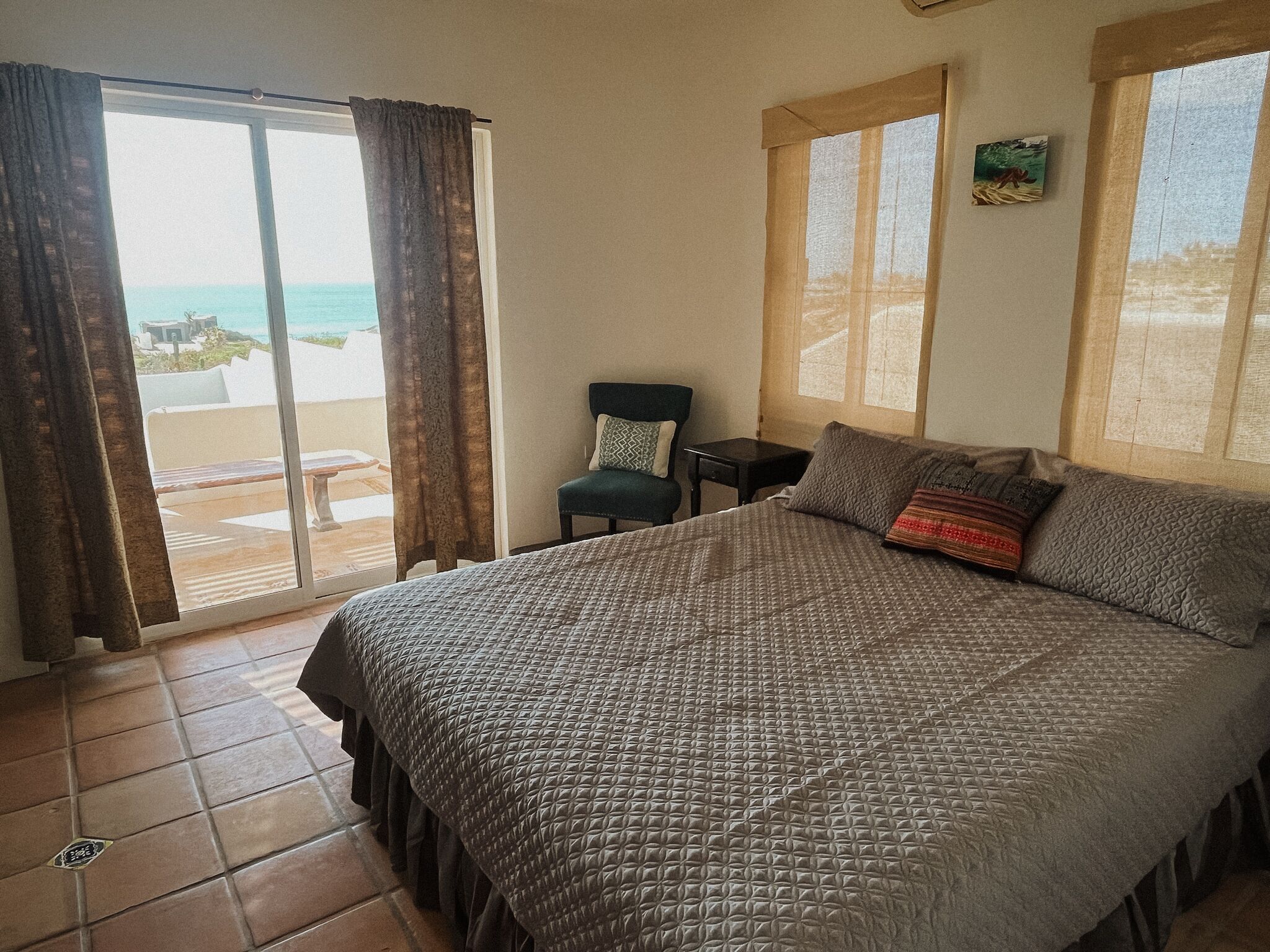 A bedroom with a bed, a chair, a small table, and a view of the beach through a large window.