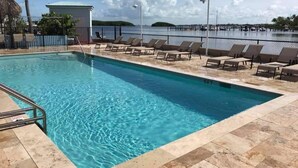 A swimming pool with clear blue water, surrounded by lounge chairs and a fence.