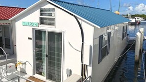 A small, white building with a blue roof, labeled "TARPO N," docked at a marina with boats in the background.