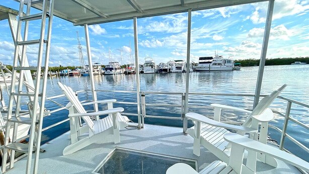 A covered deck with white chairs and a glass floor, overlooking a marina with boats.