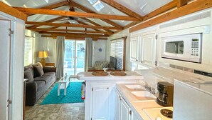 A compact kitchen with a microwave, stove, and coffee maker. There is a sofa and a small table with a lamp in the living area.