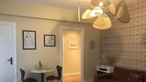 A living room with a brown sofa, two black chairs, a small round table, and a patterned rug. There are two framed artworks on the wall, a door, and a patterned wall. - Cocoon Design - Comfortable and bright - Beachfront & Golden Triangle (Deauville)