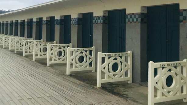 A row of white, single-room cabins with dark blue doors, each labeled with a name, on a wooden deck. - Cocoon Design - Comfortable and bright - Beachfront & Golden Triangle (Deauville)
