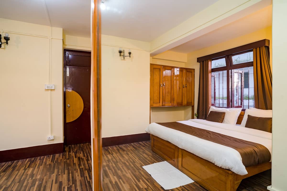 A hotel room with a large bed, wooden wardrobe, and a window with curtains.