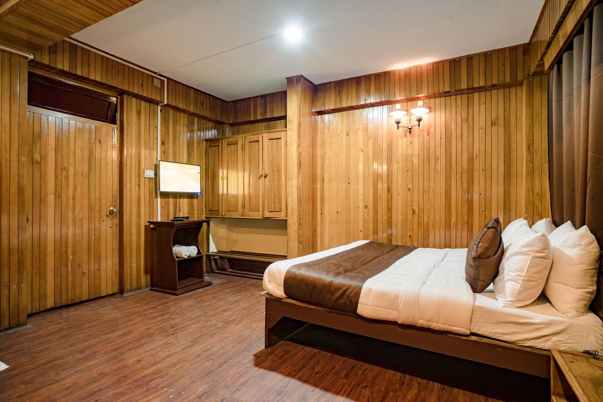 A wooden-paneled room with a bed, a desk, and a television.