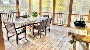A covered outdoor dining area with a wooden table and chairs, a potted plant, and a built-in sink.