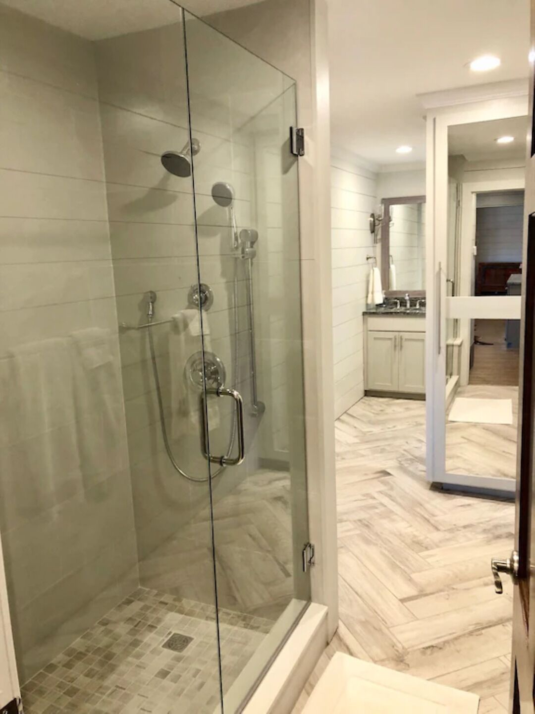 A modern bathroom with a glass-enclosed shower, a walk-in bathtub, and a visible kitchen area in the background.
