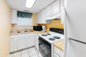 Compact kitchen with sink, microwave, stove, and refrigerator, offering a convenient space for meal preparation.