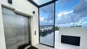 An elevator, a glass door leading to a balcony with a view of the beach, and a black mat at the entrance. - GAIA ~ One Bedroom Condo w/Pool. New Build✨ (Puerto Morelos)