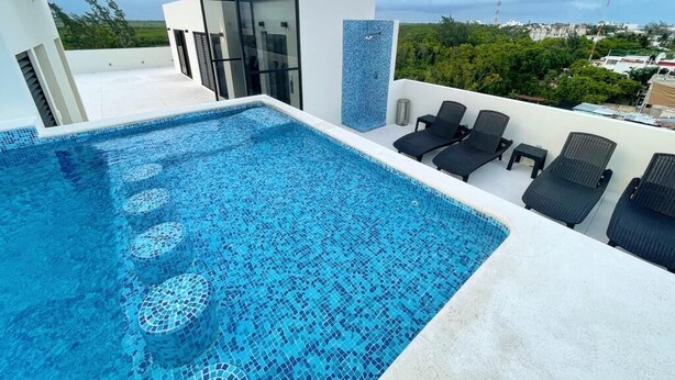 A rooftop pool with clear blue water, surrounded by lounge chairs and a glass enclosure. - GAIA ~ One Bedroom Condo w/Pool. New Build✨ (Puerto Morelos)