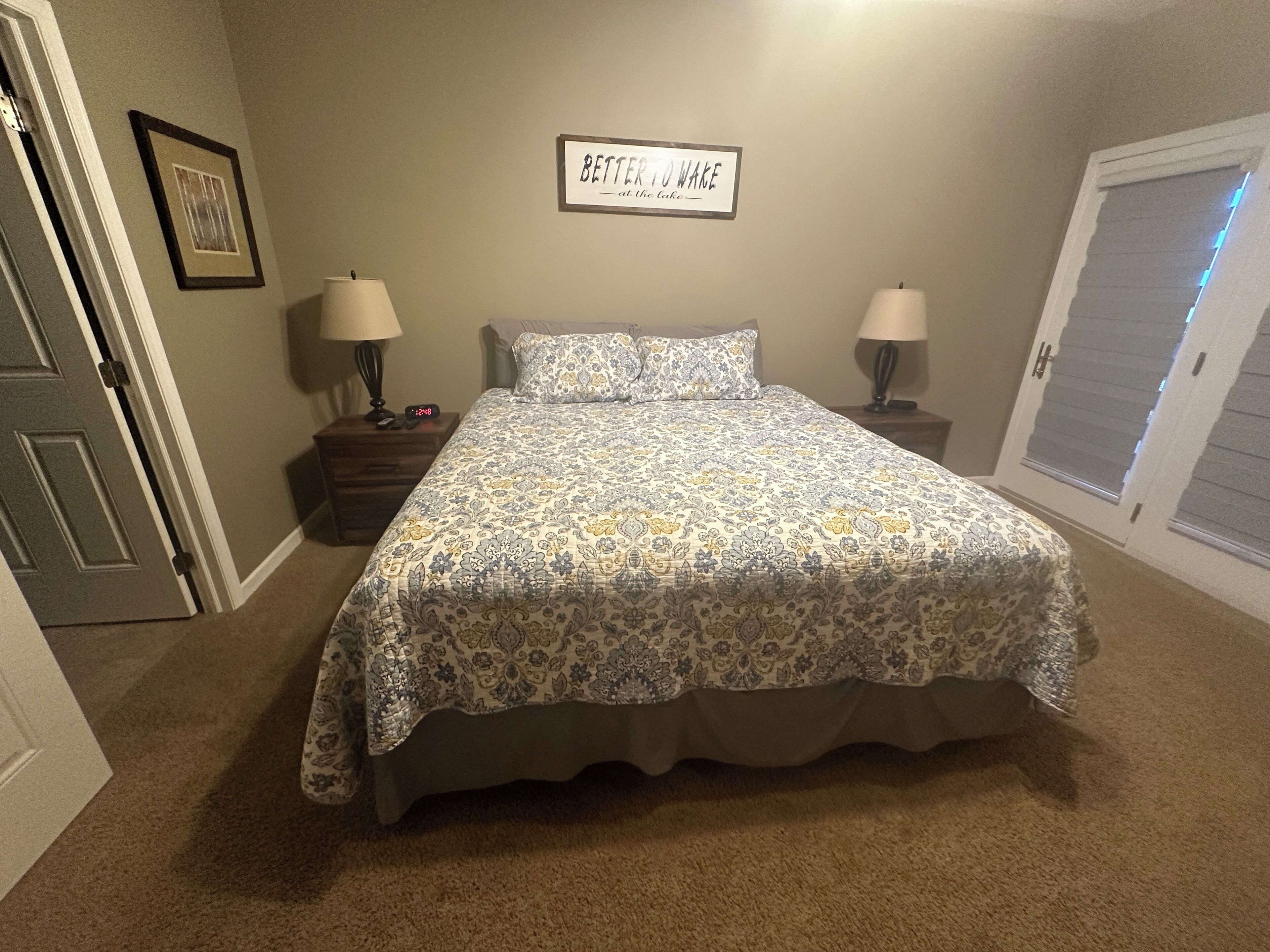 A bedroom with a bed, two bedside tables, a wall clock, and a framed sign.
