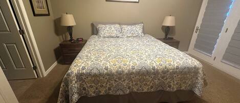 A bedroom with a bed, two bedside tables, a wall clock, and a framed sign.
