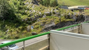 Ein Balkon mit Blick auf eine gebirgige Landschaft, eine Straße mit einem Auto und einem grünen Geländer.
