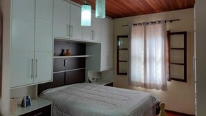 Un dormitorio con cama, armarios blancos, una estantería, una mesita de noche y una ventana con cortinas.