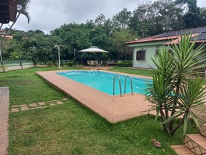 A swimming pool with a tiled deck, surrounded by grass and a few plants. - Beautiful farm with stunning views located in a charming and beautiful condominium. (São Roque)
