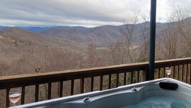 Un jacuzzi con una copa de vino en una terraza de madera con vistas a un paisaje montañoso.