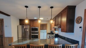 Una cocina con armarios de madera, encimera de granito y cuatro sillas de madera.