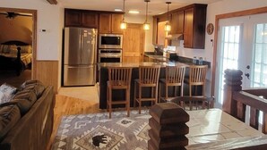 Una cocina con armarios de madera, un refrigerador, un horno y un comedor con sillas y una mesa.