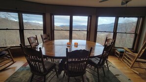 Una mesa redonda de comedor con seis sillas de madera, ventanas amplias con vista a la montaña y ventiladores de techo.