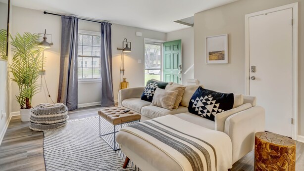 A modern living room with a sofa, ottoman, and a round wooden side table.