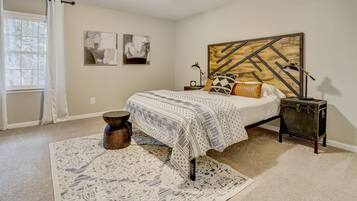 A bedroom with a bed, a headboard, a nightstand, a lamp, a suitcase, and a window with curtains.