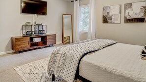 A bedroom with a bed, a TV, a dresser, and two abstract paintings.