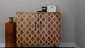 A room with a patterned cabinet, a framed artwork, and a small potted plant on the cabinet.