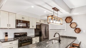 A modern kitchen with white cabinets, stainless steel appliances, a granite countertop, and a hexagonal wooden backsplash. - Stunning & Glamorous 3BR-3BA - Sleep 10! (Philadelphia)