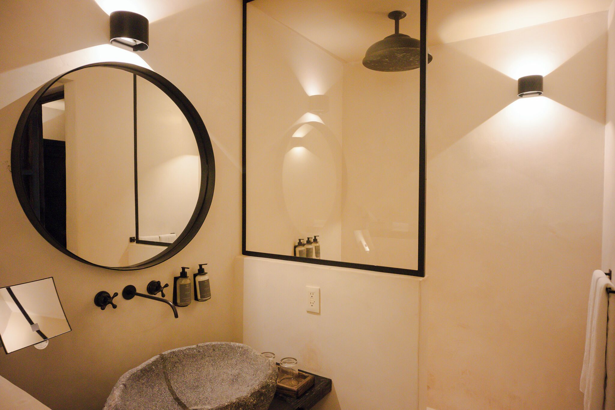 A bathroom with a round mirror, a rectangular mirror, a stone basin, and a towel rack.