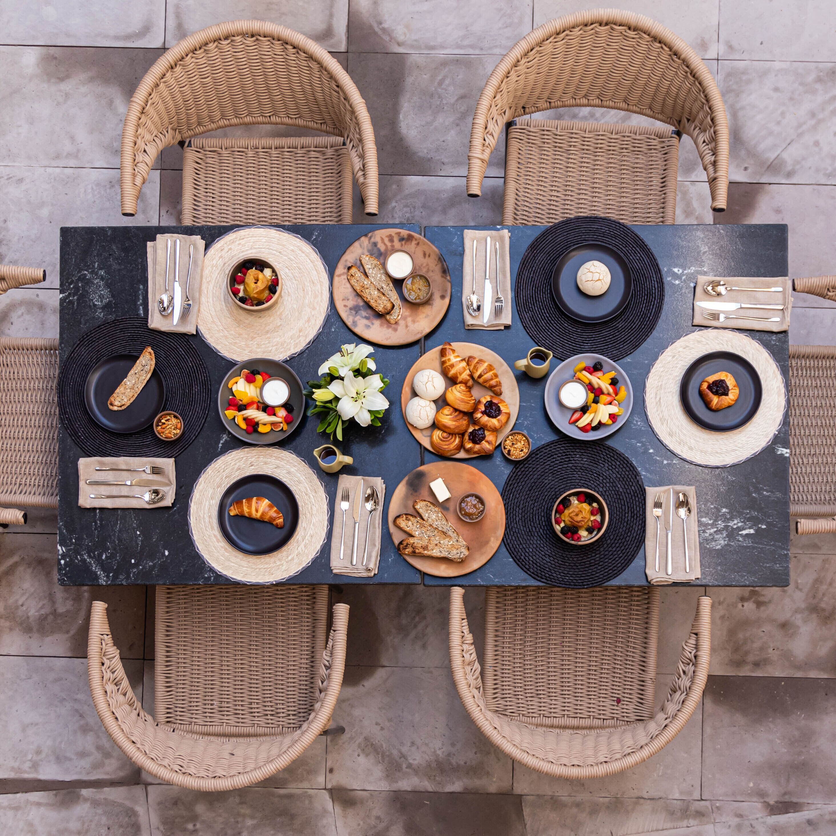 A dining table with wicker chairs, surrounded by plates of food, utensils, and napkins.