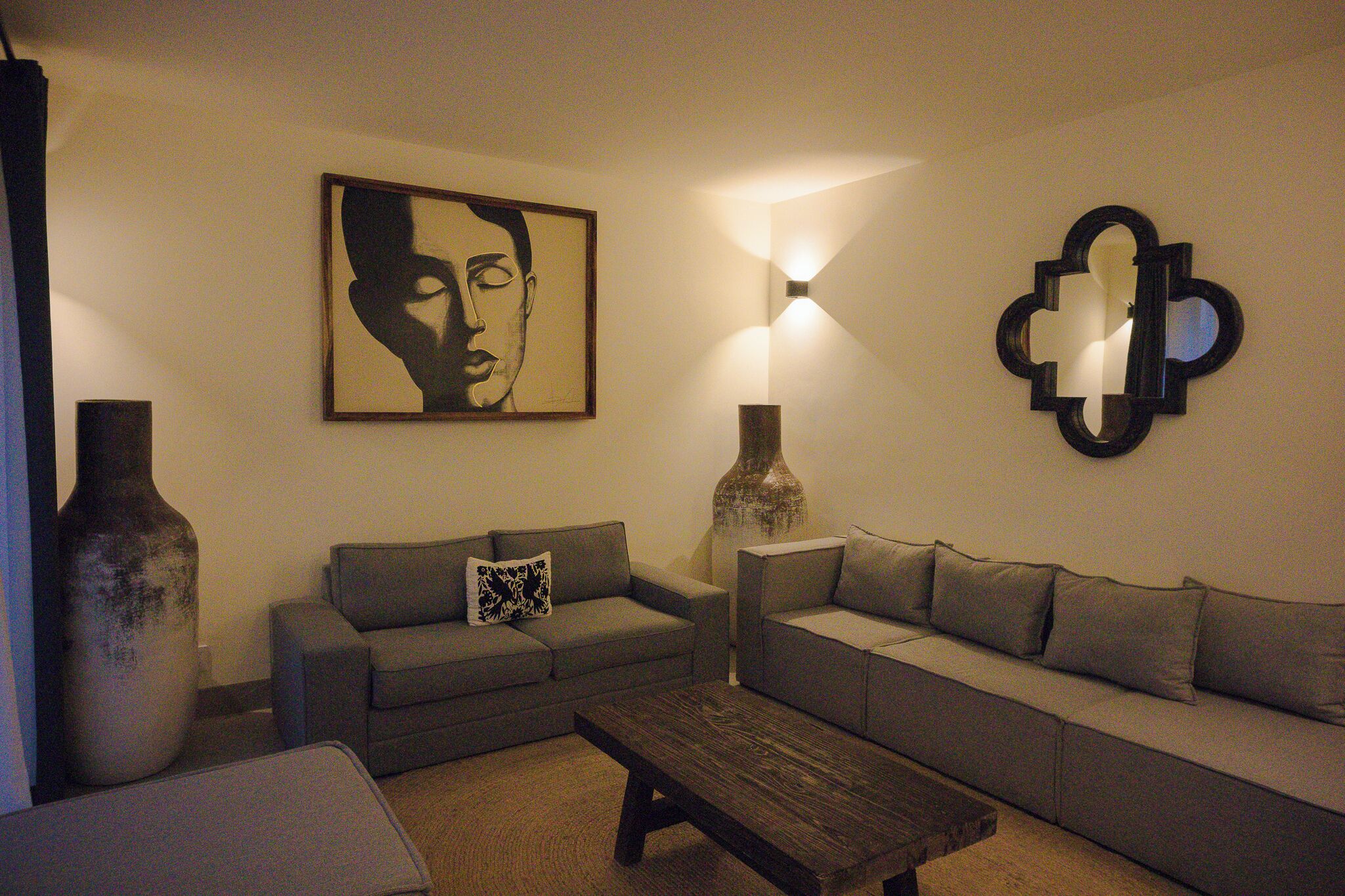 Ein Wohnzimmer mit zwei Sofas, einem Couchtisch, einer großen Vase und Wandleuchten.