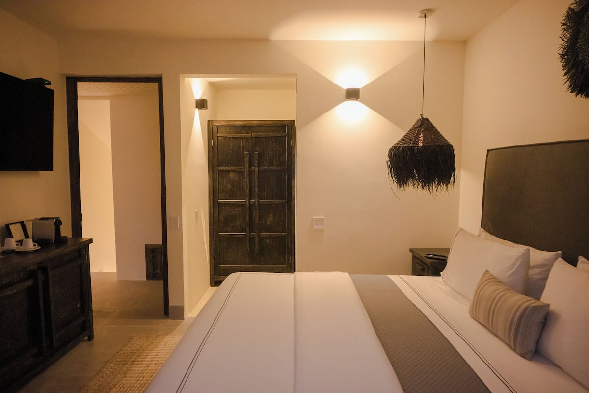 A hotel room with a large bed, a wooden door, a small bedside table, and a wall-mounted TV.