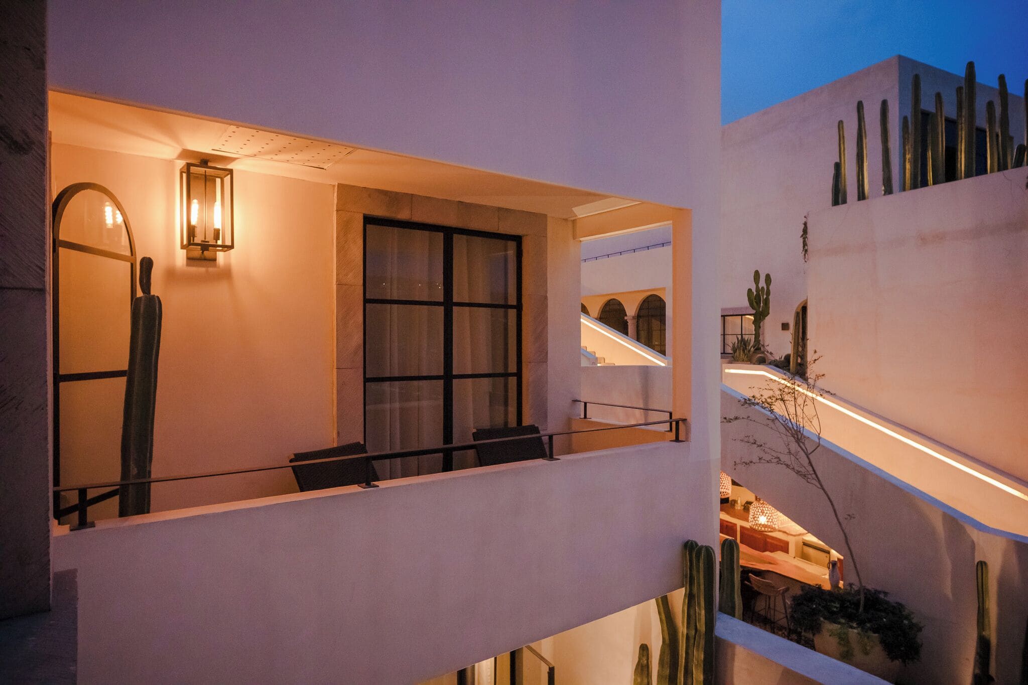 Un edificio moderno con balcón, un ventanal grande y un jardín de cactus.