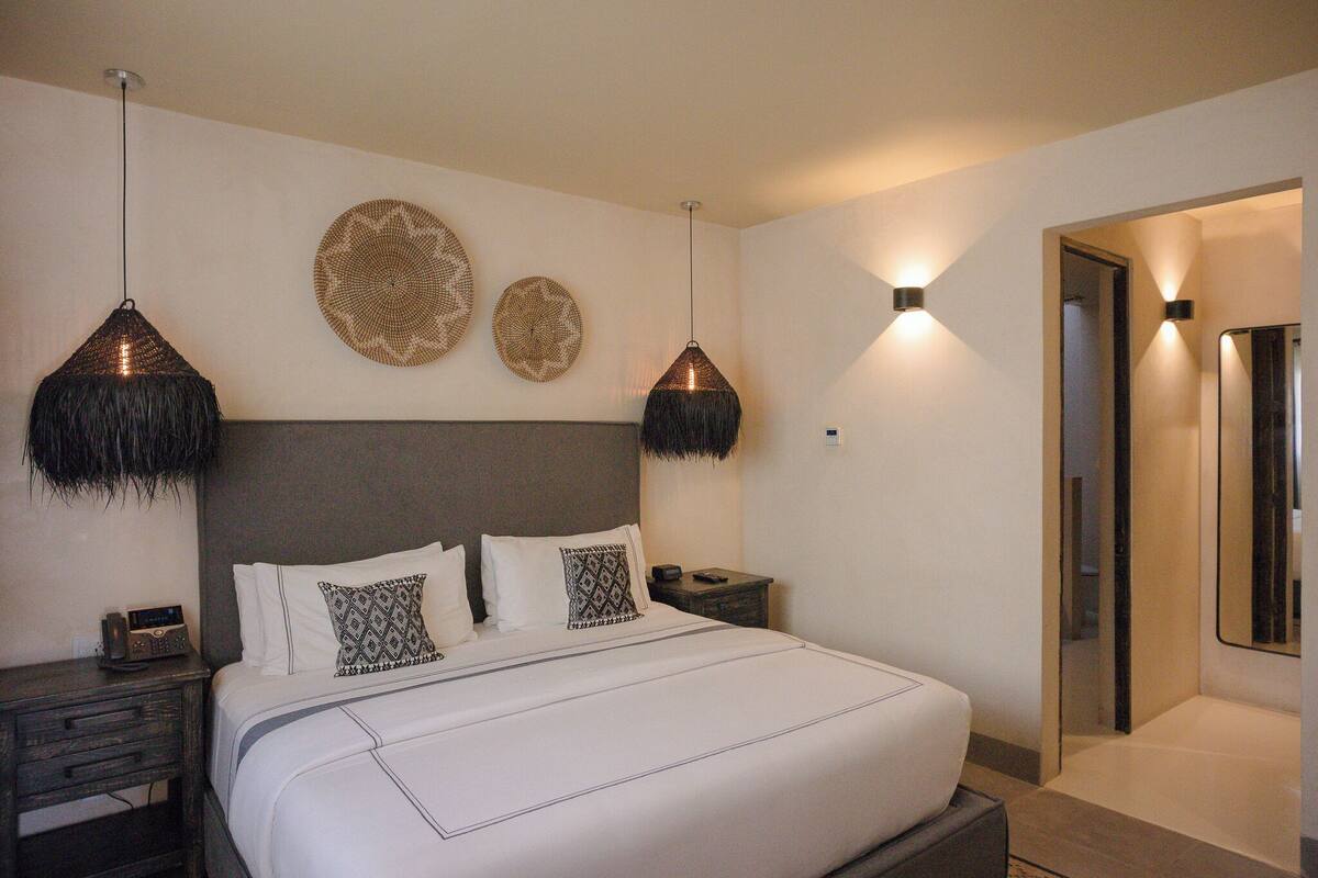 A modern hotel room with a large bed, two wall-mounted lamps, and a mirror.
