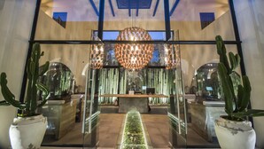 A reception area with a central desk, glass partitions, cacti, and a modern chandelier. - Hotel Amatte San Miguel de Allende (San Miguel de Allende)