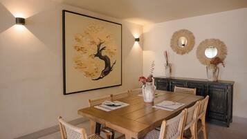 A dining area with a wooden table, wicker chairs, a vase with flowers, and wall-mounted decor.