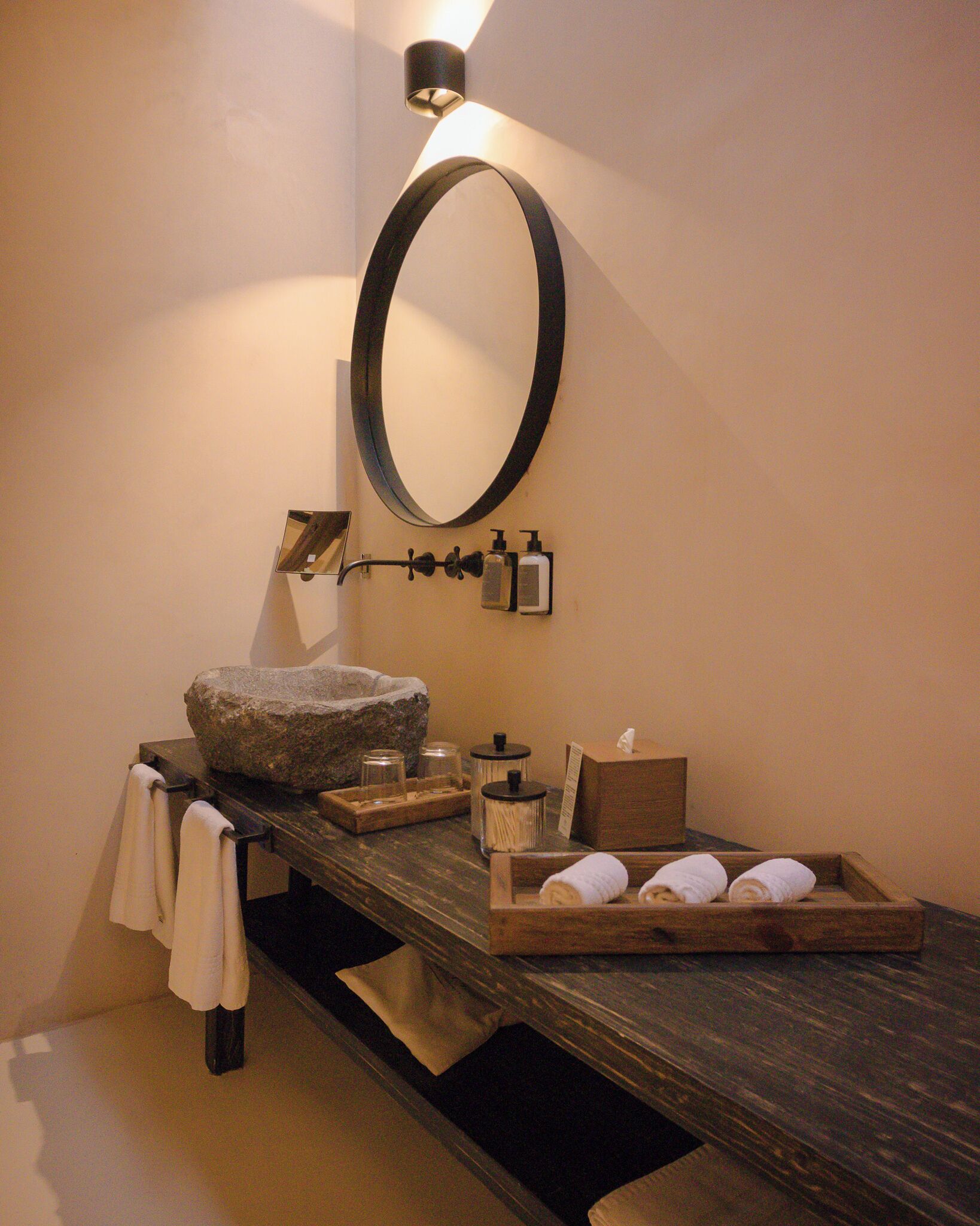 A bathroom with a stone sink, a wooden tray with towels, and a large mirror.