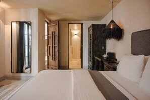Una habitación de hotel con una cama grande, un armario, un escritorio con lámpara y un espejo.