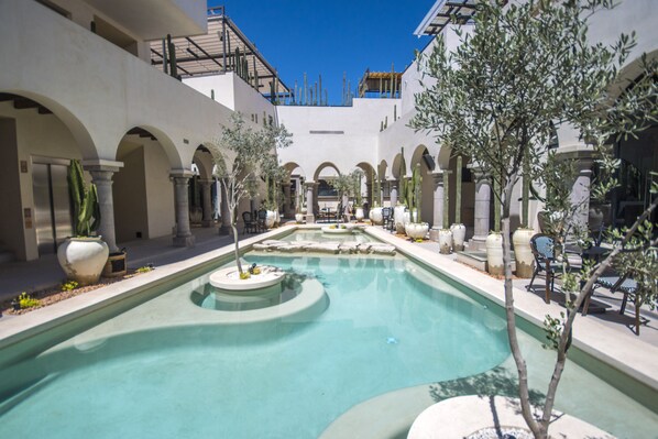 Un patio con piscina, zonas de estar y cactus.