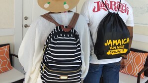 Una persona portant un barret de palla i una camisa blanca amb la paraula “Jamaica” escrita al darrere, subjecte una bossa negra amb la inscripció “Jamaica” i “Yuh Nice”. 