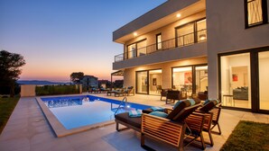 Une maison moderne à deux étages, dotée d’une piscine, d’un espace salon extérieur et d’un balcon.