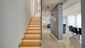 Un intérieur moderne avec un escalier en bois, un coin repas avec des chaises et un mur orné de tableaux encadrés.